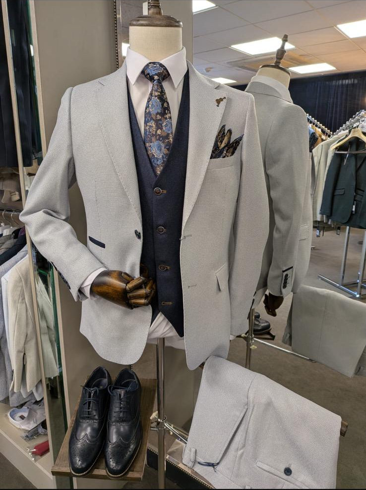 Light gray suit on a mannequin with a patterned tie and pocket square in a store setting.